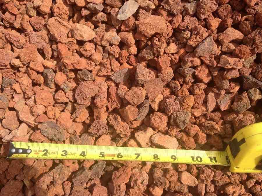 Yellow measuring tape stretched across a pile of reddish gravel stones.