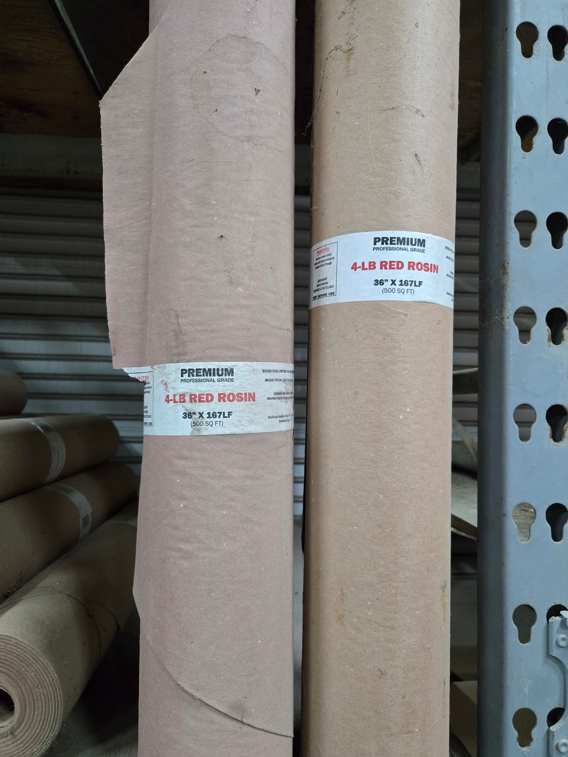 Two rolled carpets in a shop, one gray and one beige, with labels on them.