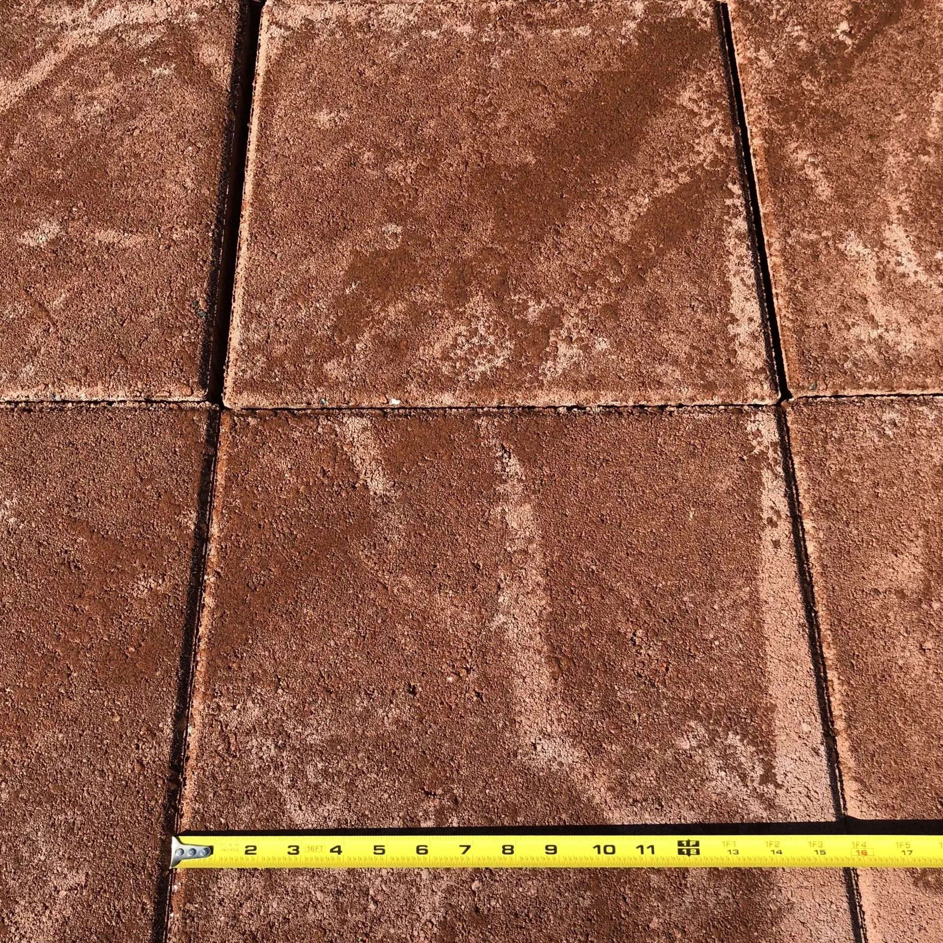 Measuring tape laid across brown tiled pavement with a grid of grout lines