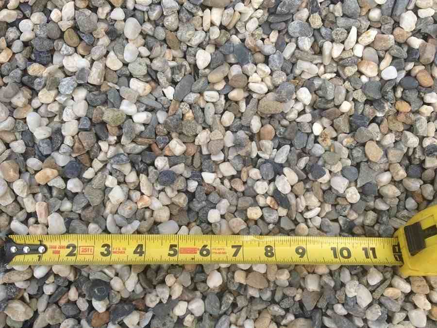 Yellow tape measure lying across small gray pebbles, showing measurements in inches.