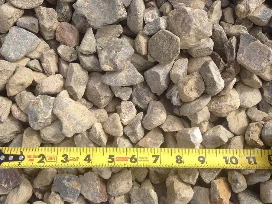Close-up of tan gravel stones with a yellow measuring tape stretched along the bottom edge.