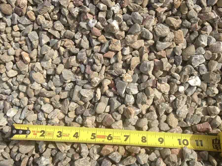 Close-up of small tan and gray gravel with a yellow measuring tape along the bottom edge.