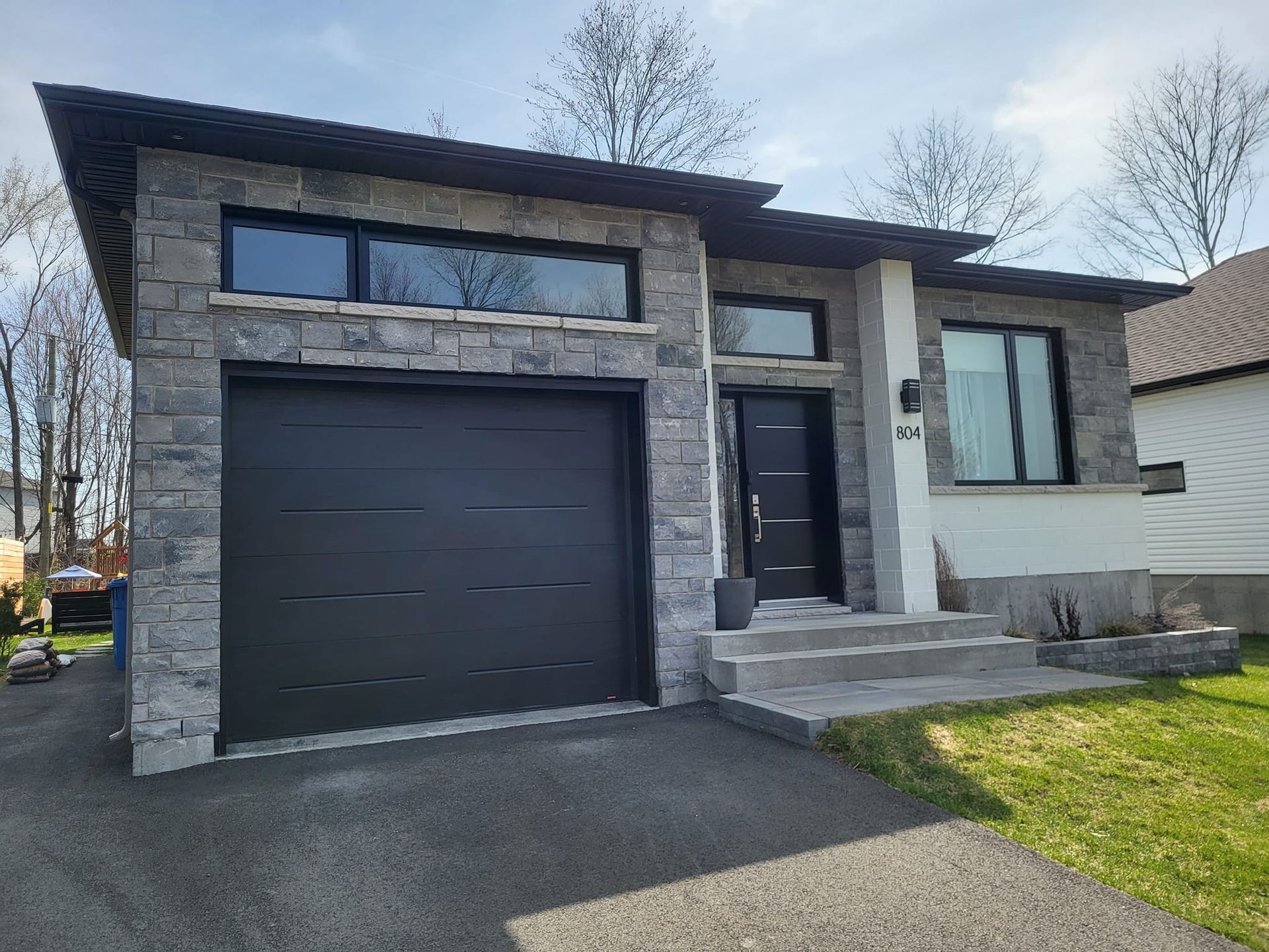 Une maison avec une porte de garage noire et des escaliers devant.