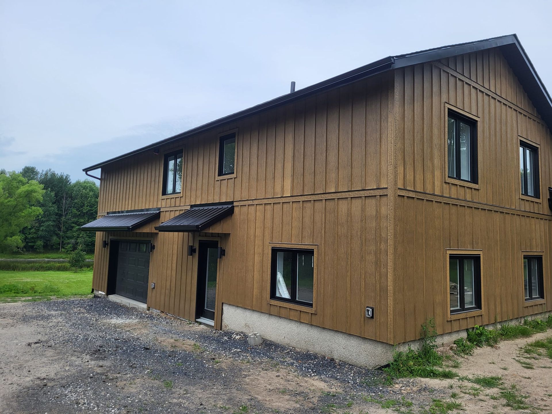 Une grande maison en bois avec un garage est située au milieu d'un champ.