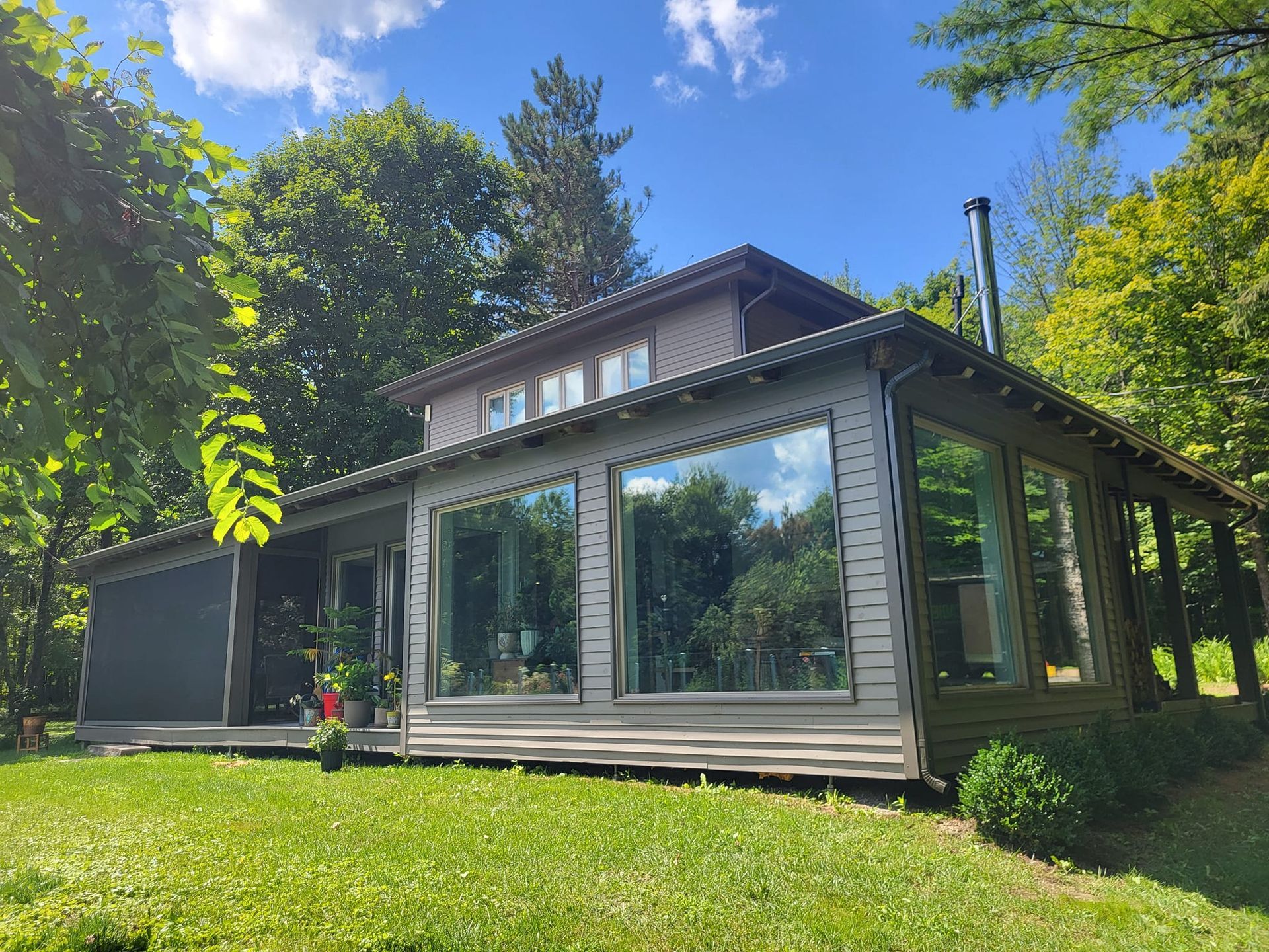 Une maison avec beaucoup de fenêtres est entourée d'arbres et d'herbe.
