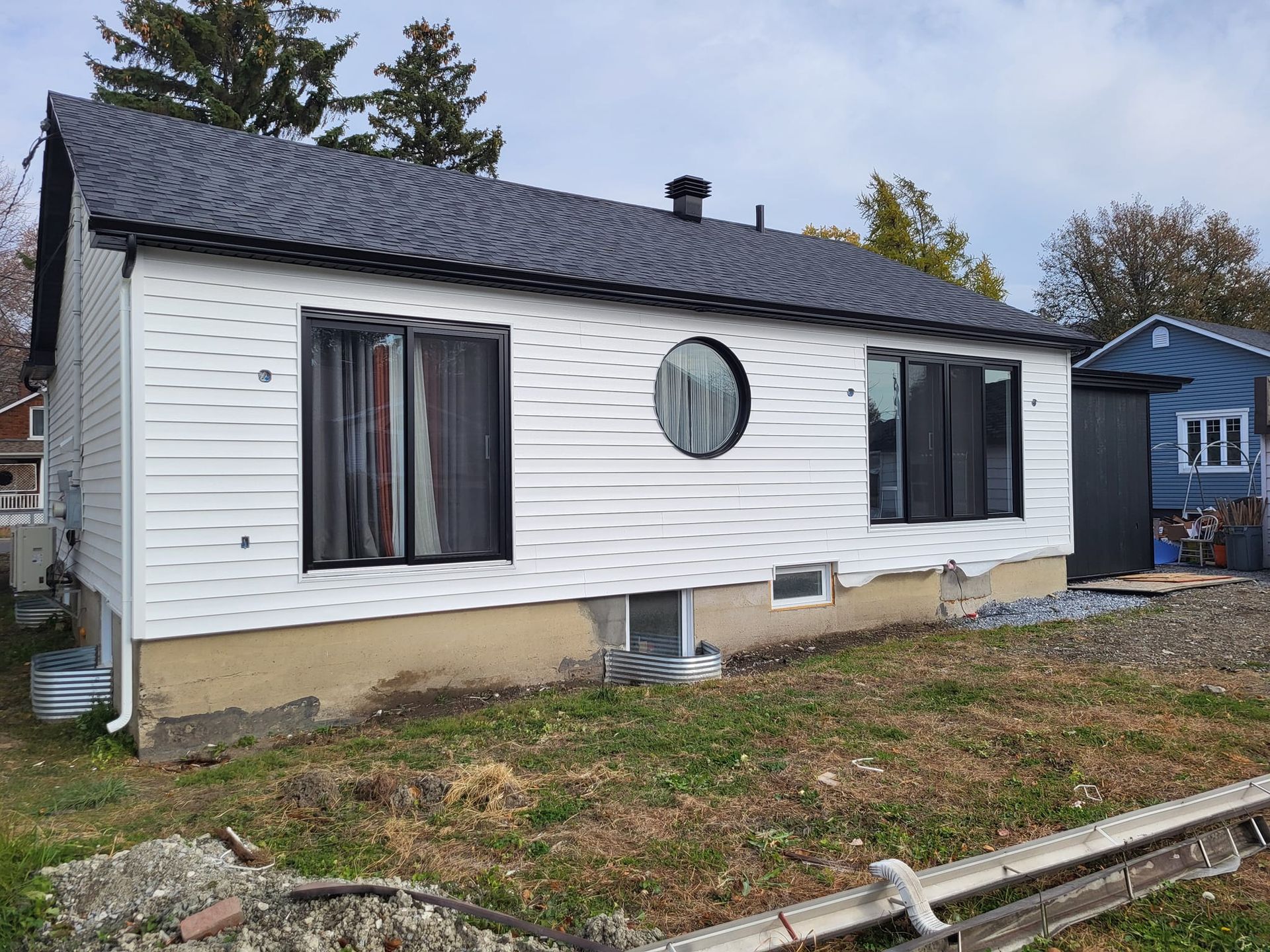 Une petite maison blanche avec un toit noir et une fenêtre ronde.