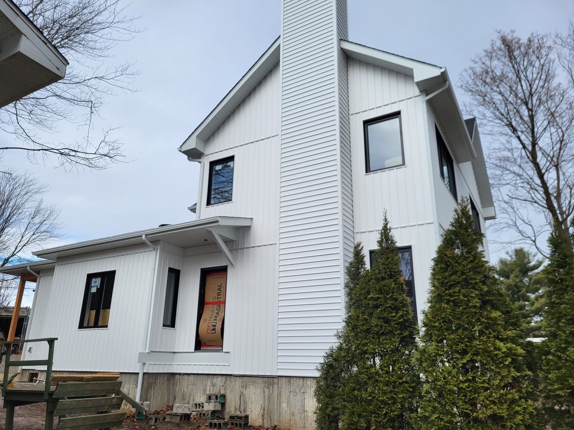 Une maison blanche avec une cheminée et des arbres devant.