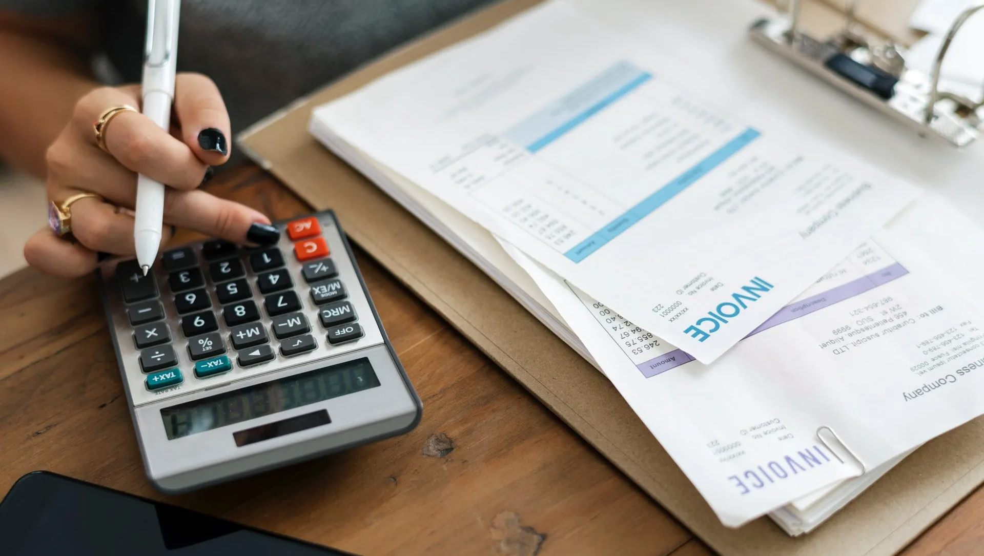 A woman is using a calculator and writing on a clipboard.