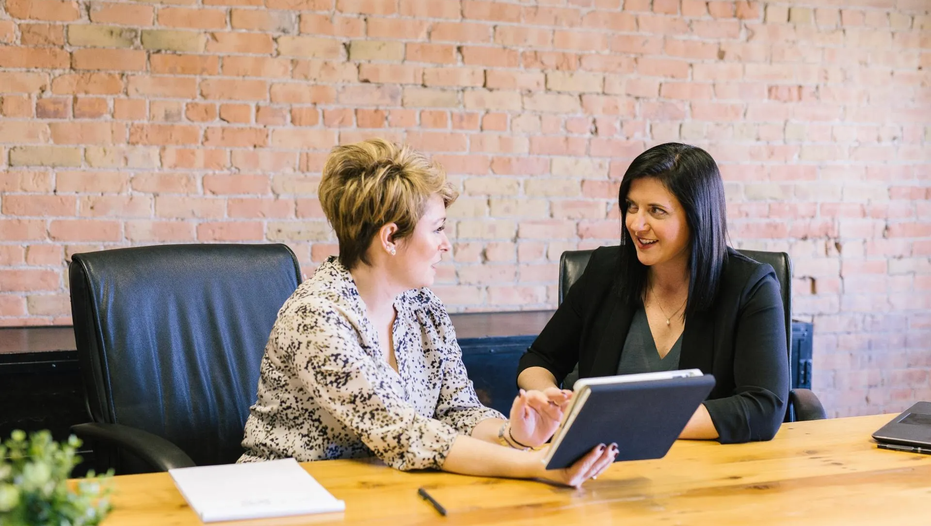 Two women are sitting at a table looking at a tablet.