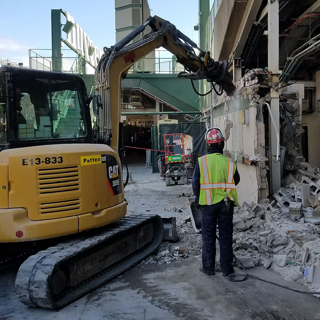 A man in a yellow vest is standing in front of a cat excavator