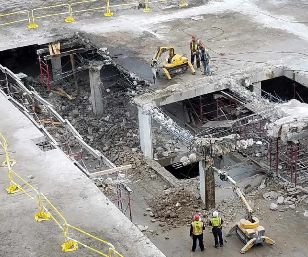 A group of construction workers are standing on top of a demolished building.
