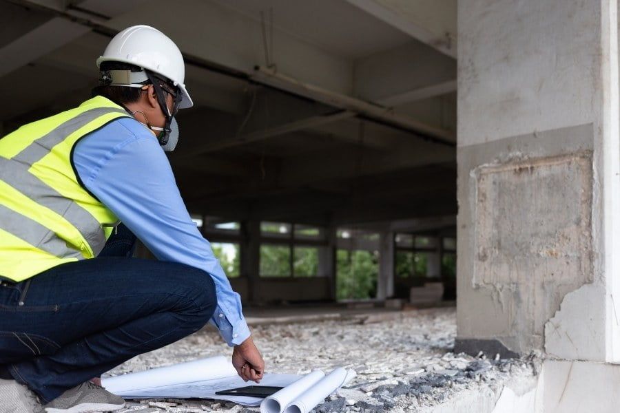 Construction worker in hard hat and safety vest inspecting debris inside a damaged building