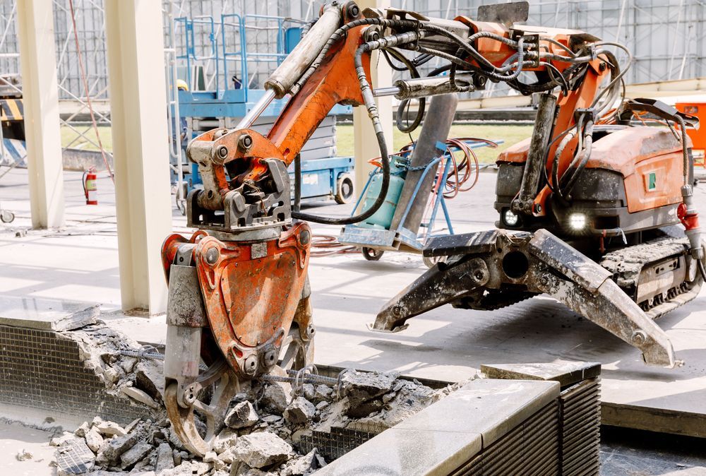 Foundation demolition with robotic equipment breaking and removing concrete floor in active construction zone
