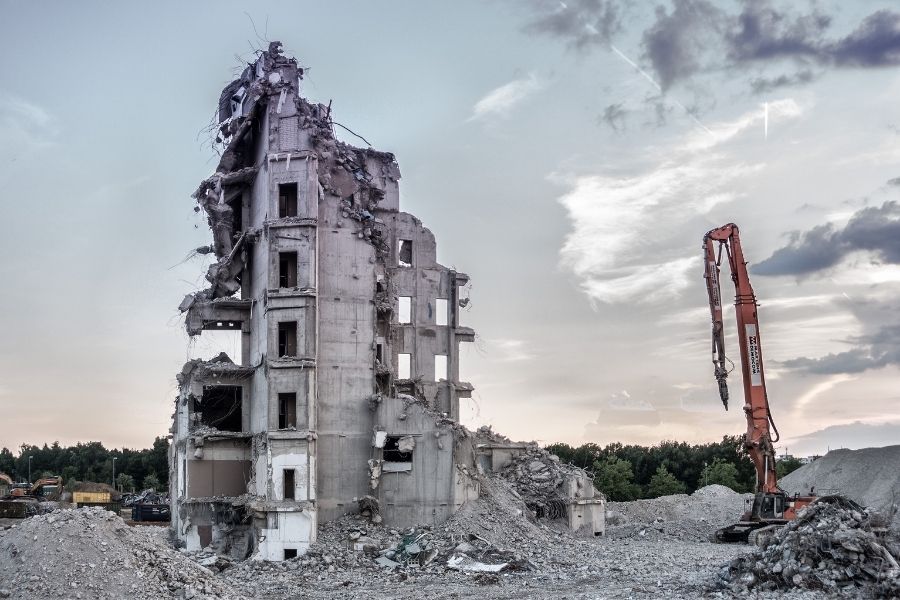 A large building is being demolished with a crane in the foreground.