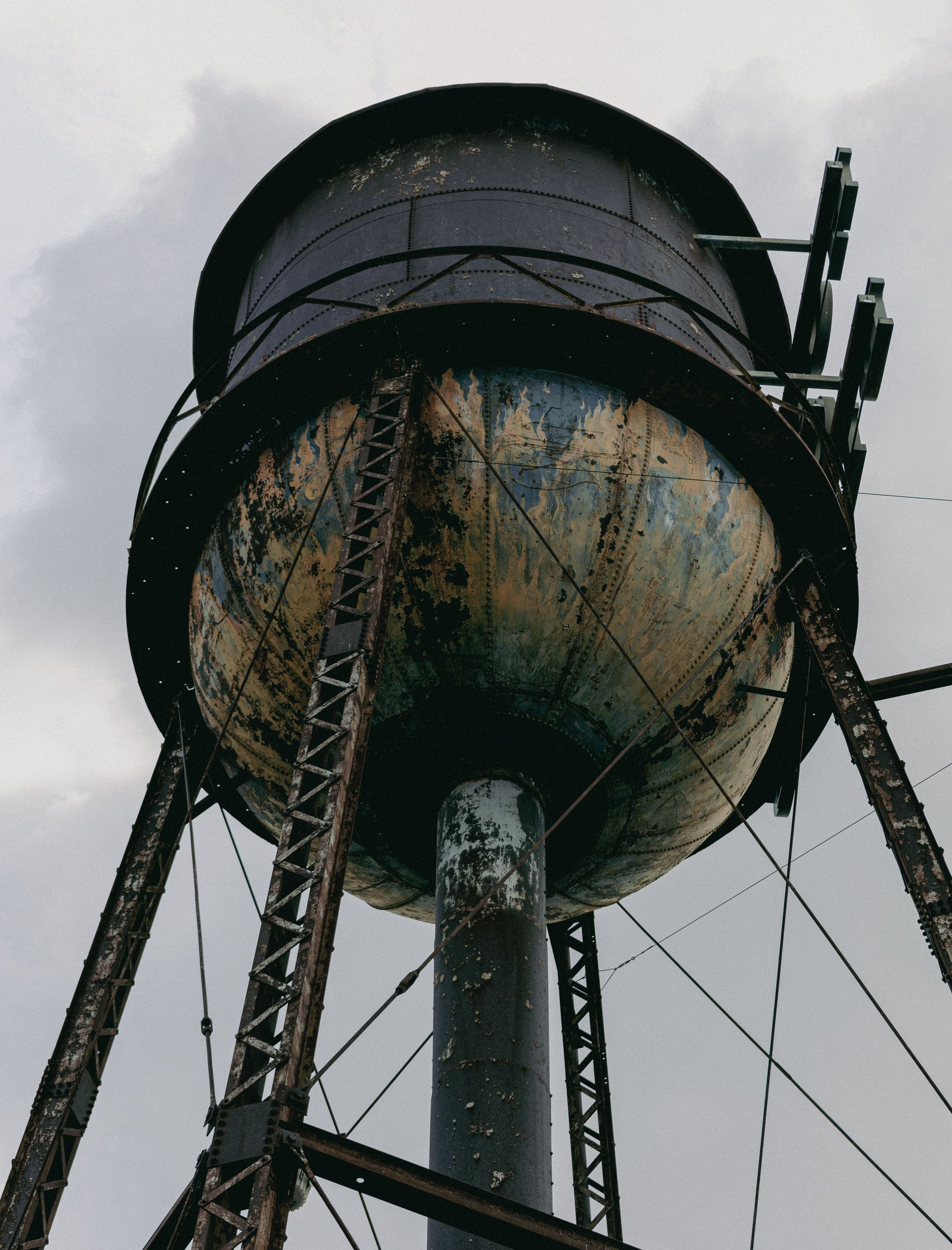 Rust-streaked water tower viewed from below against a cloudy sky
