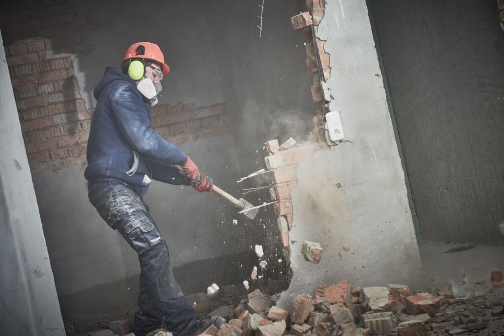 A man is breaking a brick wall with a hammer.