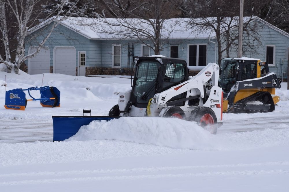 A snow plow is clearing snow from a driveway in front of a house.