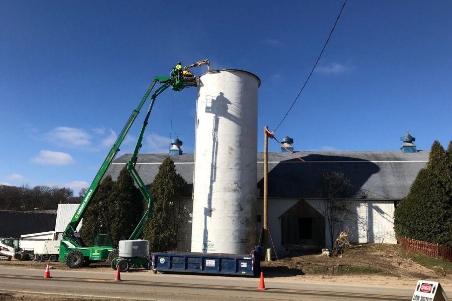 A large white silo is being painted by a crane.