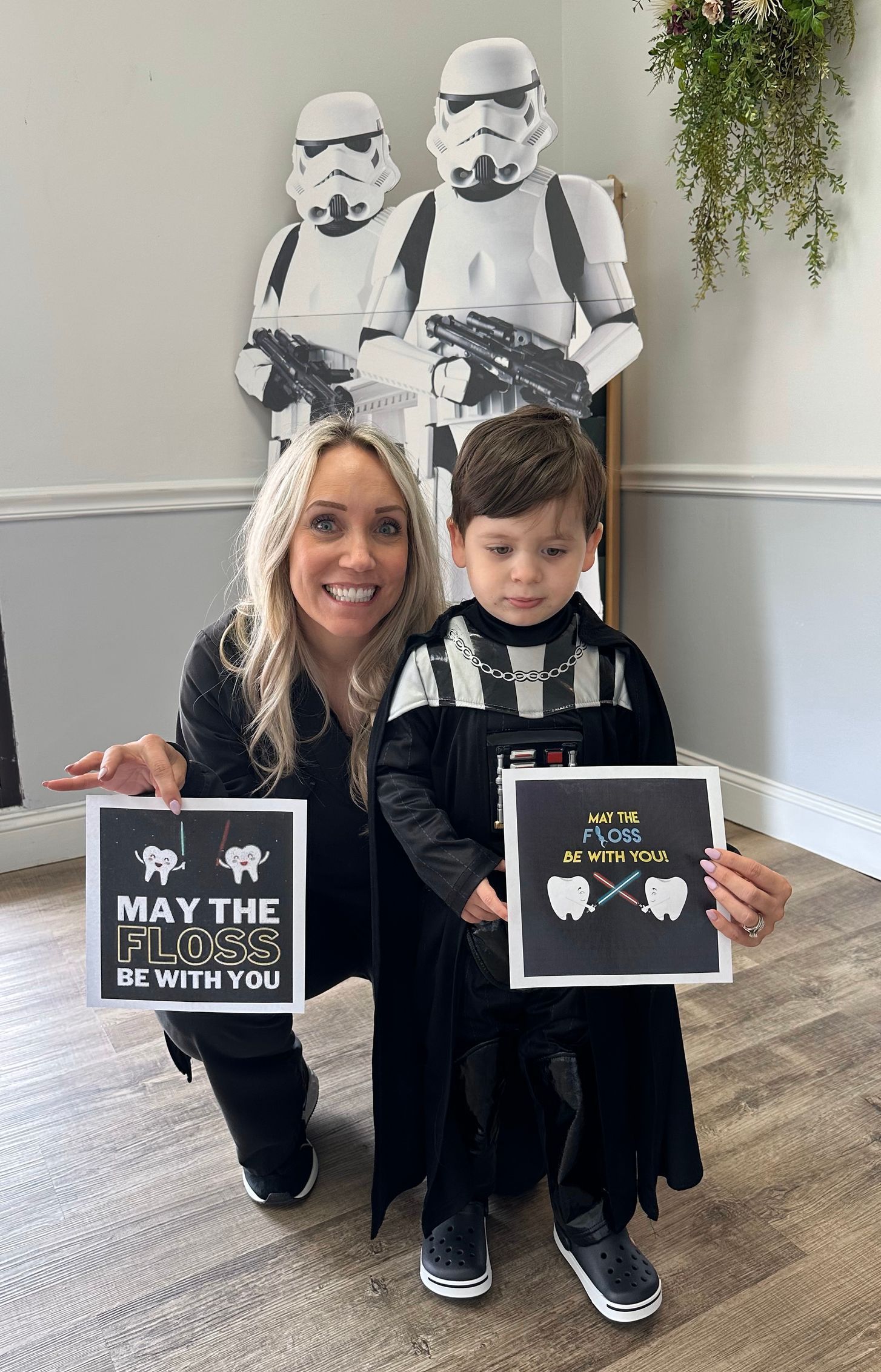 Woman and child holding May the 4th signs, posing before two Stormtrooper figures.