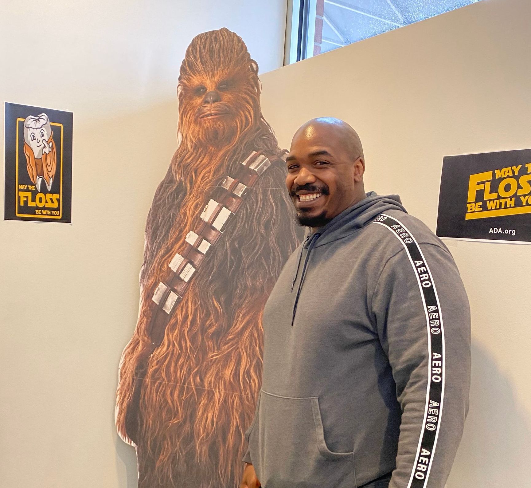 Man smiling beside a Chewbacca cutout in a hallway with Star Wars posters