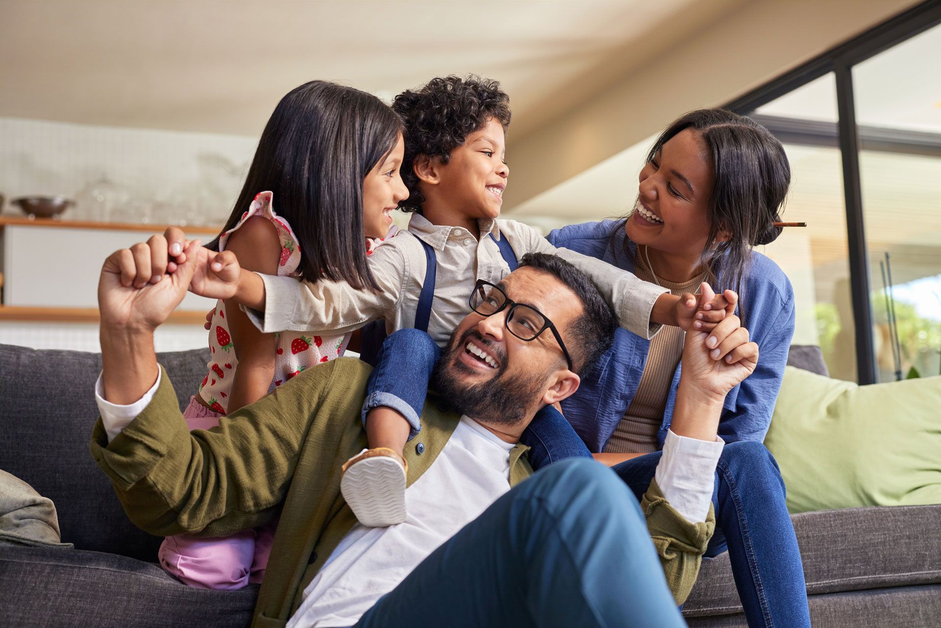Family sitting together on a couch, smiling and playing in a bright living room.