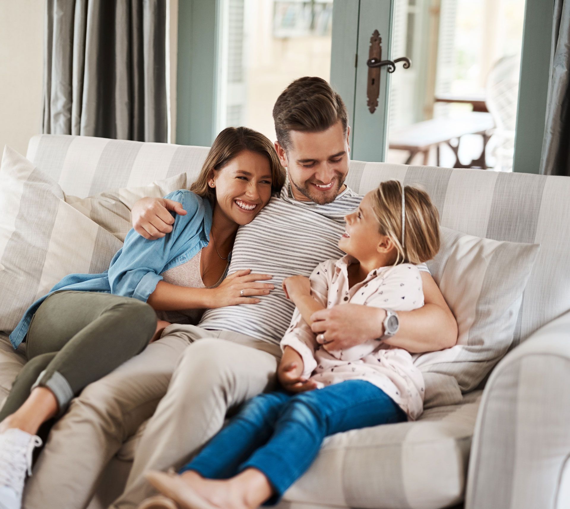 Family cuddling on a couch, smiling and relaxing in a bright living room.