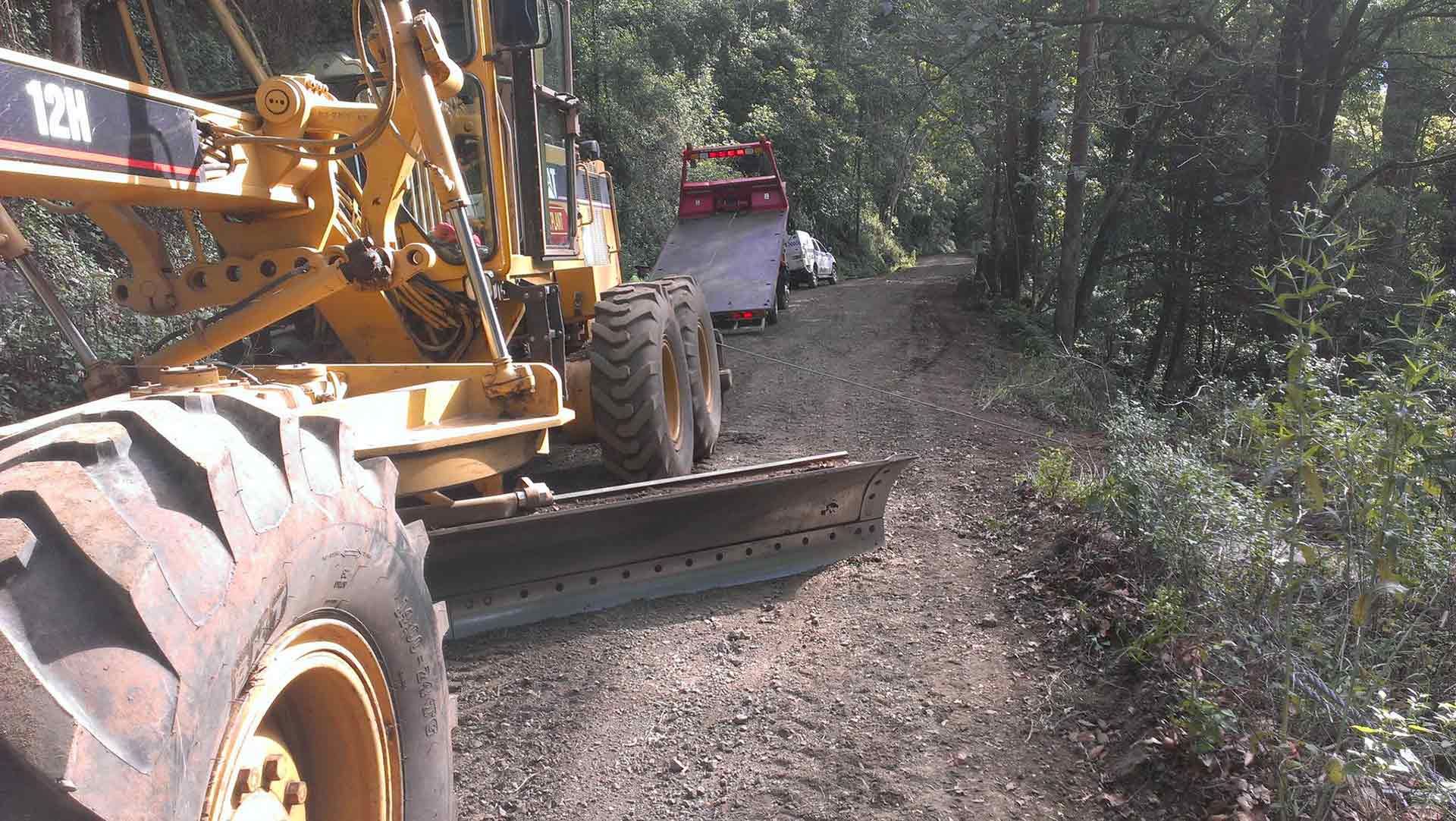 A Caterpillar Tractor Is Driving Down a Dirt Road — Alpine Towing Services in Lismore, NSW

