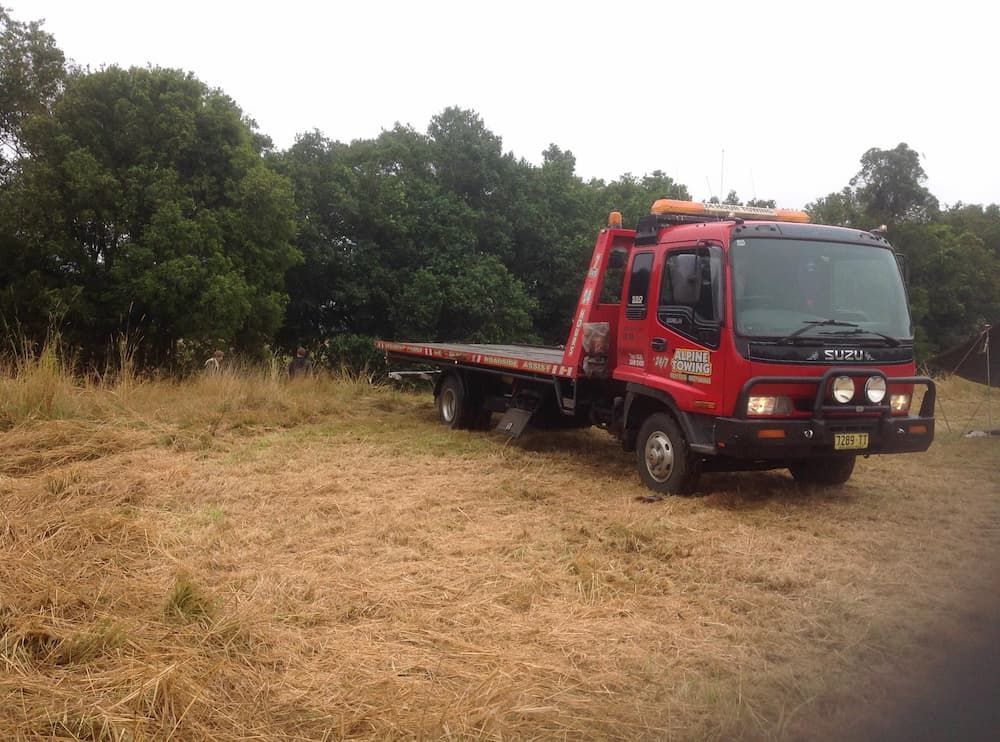 A Red Tow Truck Is Parked in A Field with Trees in The Background — Alpine Towing Services in Lismore, NSW