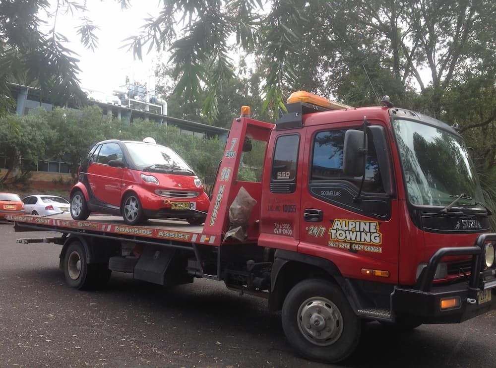 A Red Tow Truck Is Towing a Smart Red Car — Alpine Towing Services in Lismore, NSW