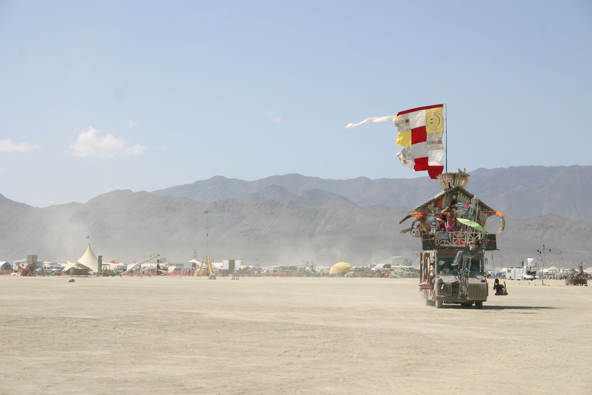 Decorated mobile shrine or vehicle with colorful flags on a dusty desert plain, mountains in the background