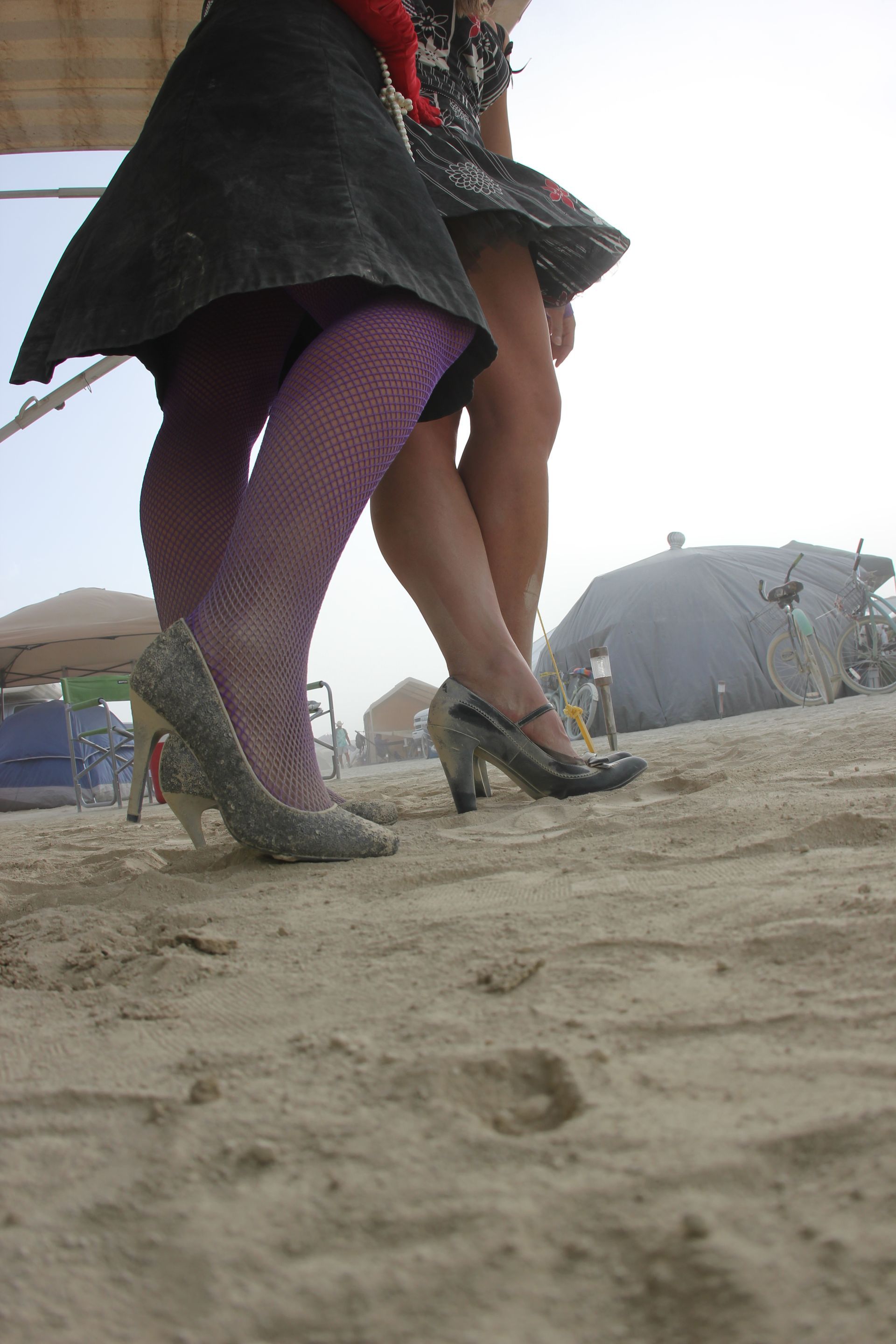 Two dancers in skirts and tights step on dusty ground, with tents in the background.