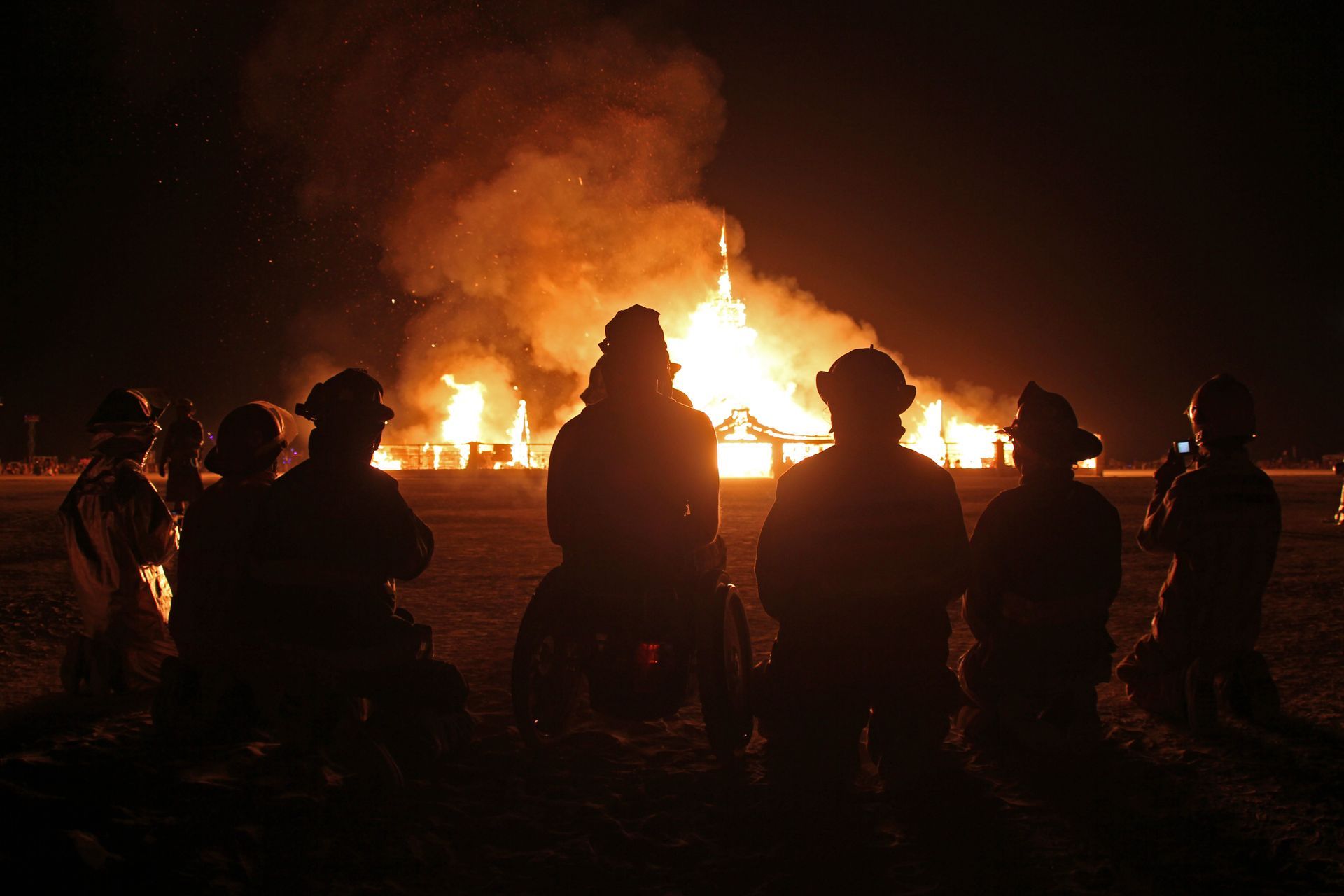 Silhouetted firefighters facing a large blaze at night