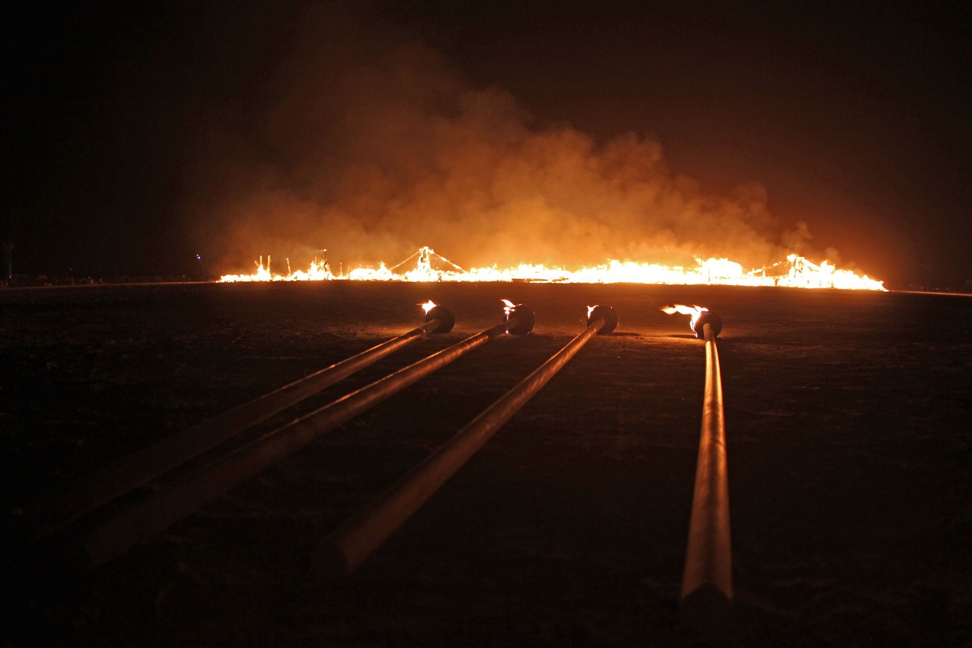 Nighttime blaze across a field, with bright orange flames and smoke on the horizon