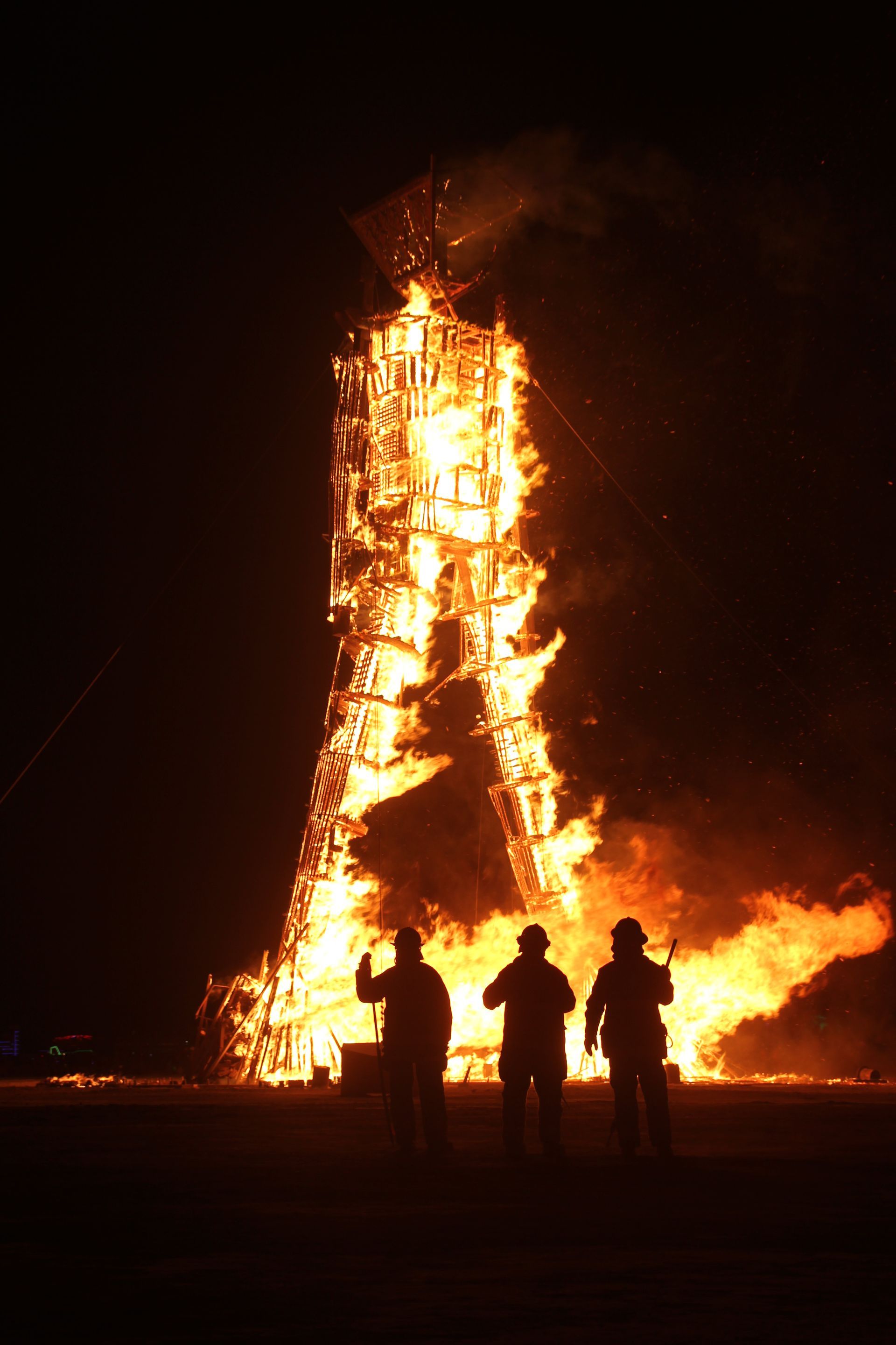 Silhouetted people watching a large burning tower at night