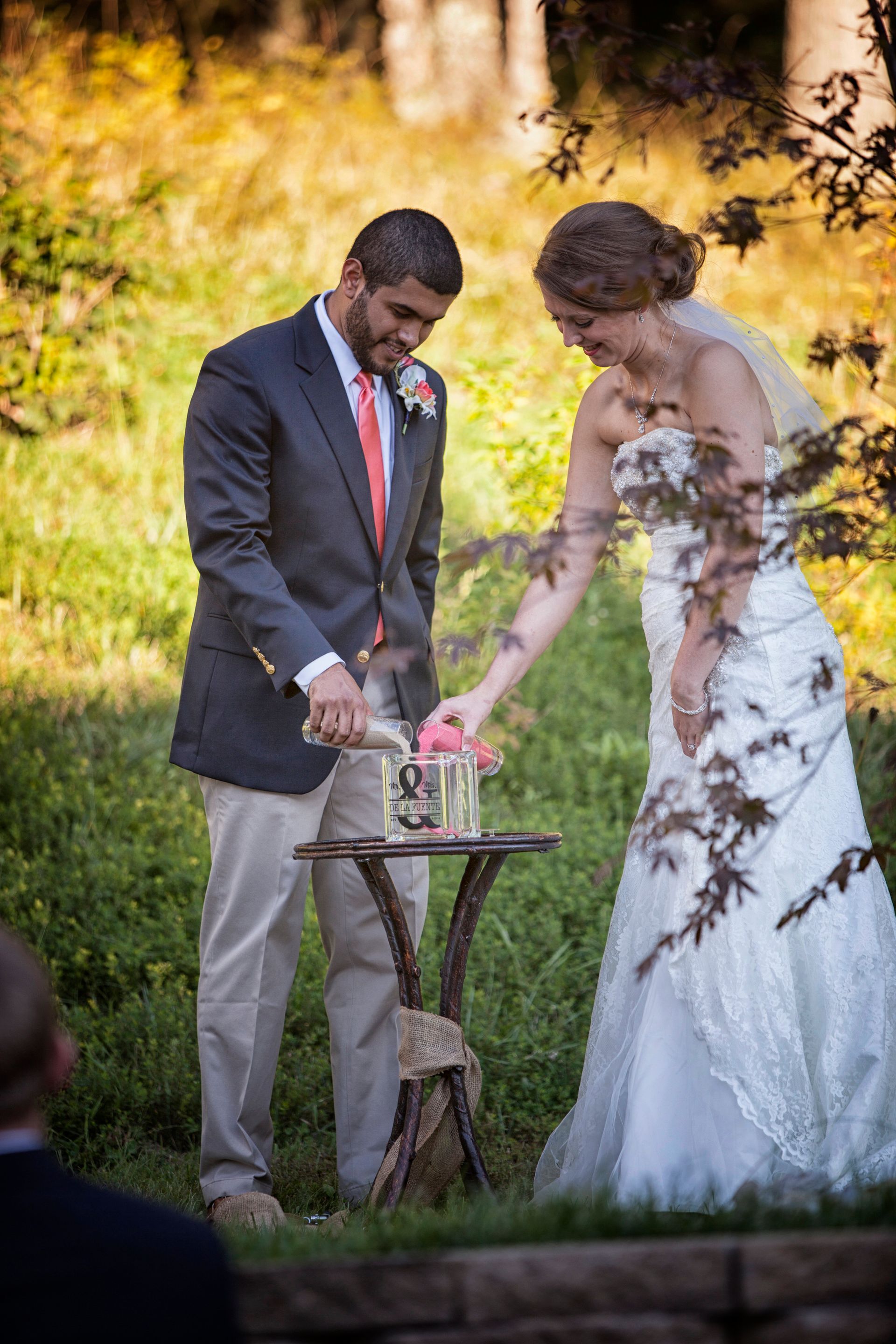 Bride and groom cut a wedding cake outdoors beside a small round table.