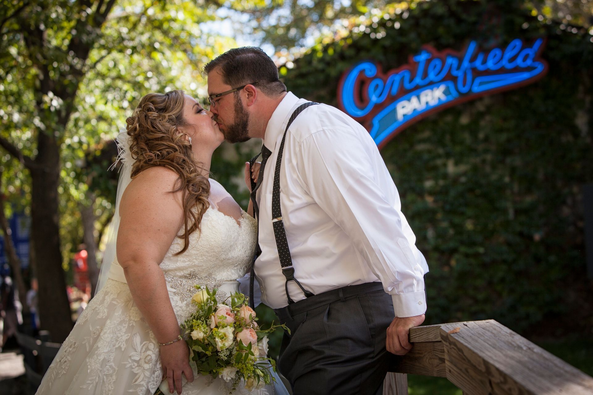 Couple kissing in wedding attire near a blue Centerville Park sign outdoors