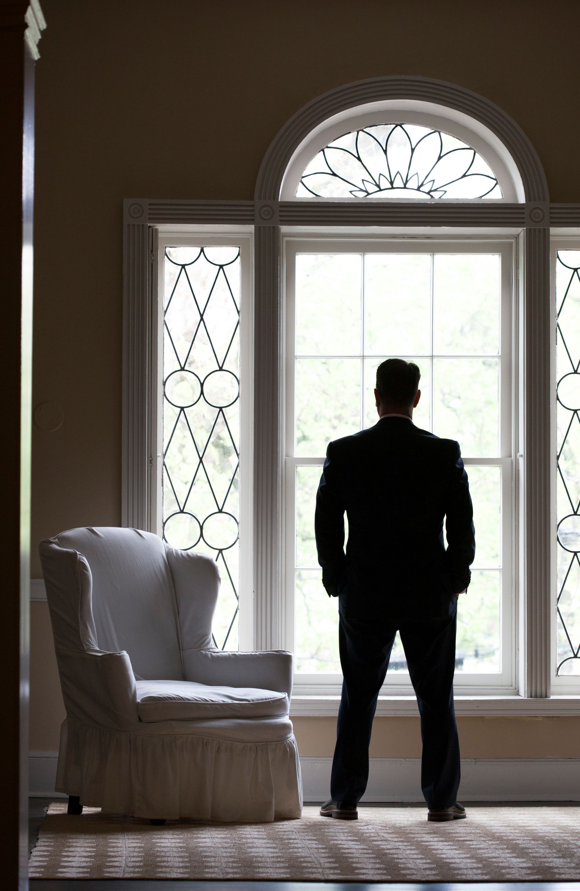 Person standing in front of a large bright window beside a white armchair