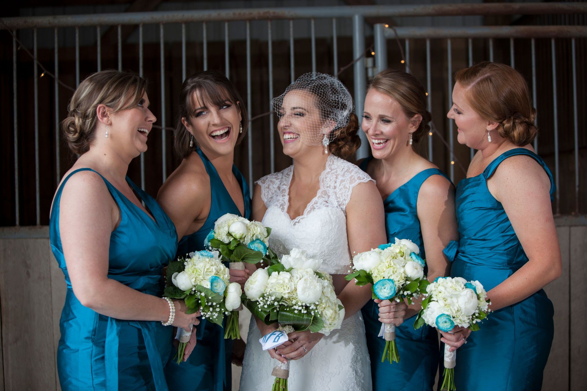 Bridesmaids in teal dresses stand with a smiling bride in white, each holding white and teal bouquets.