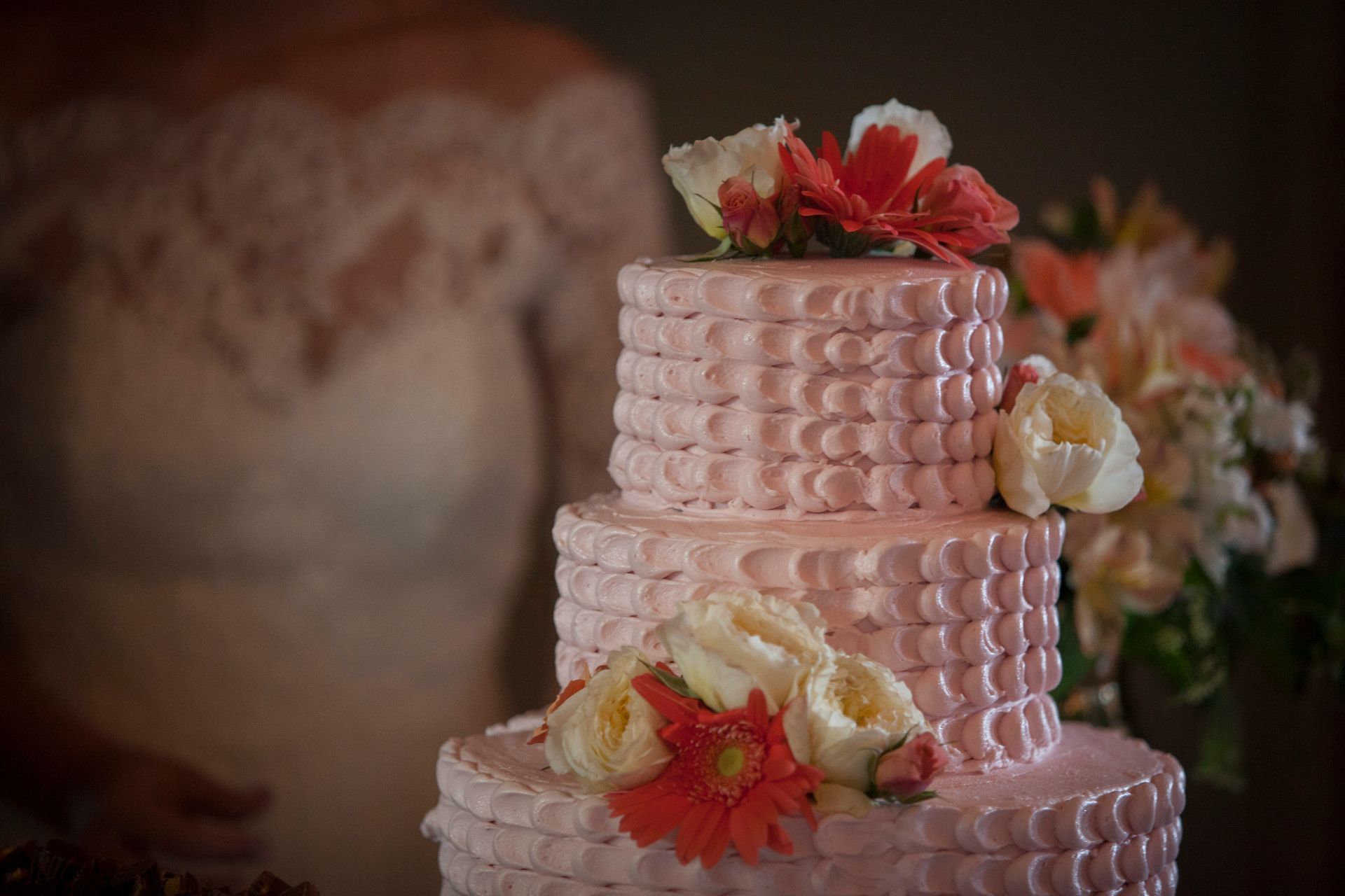 Pink tiered cake with white flowers and red accents on a decorated table