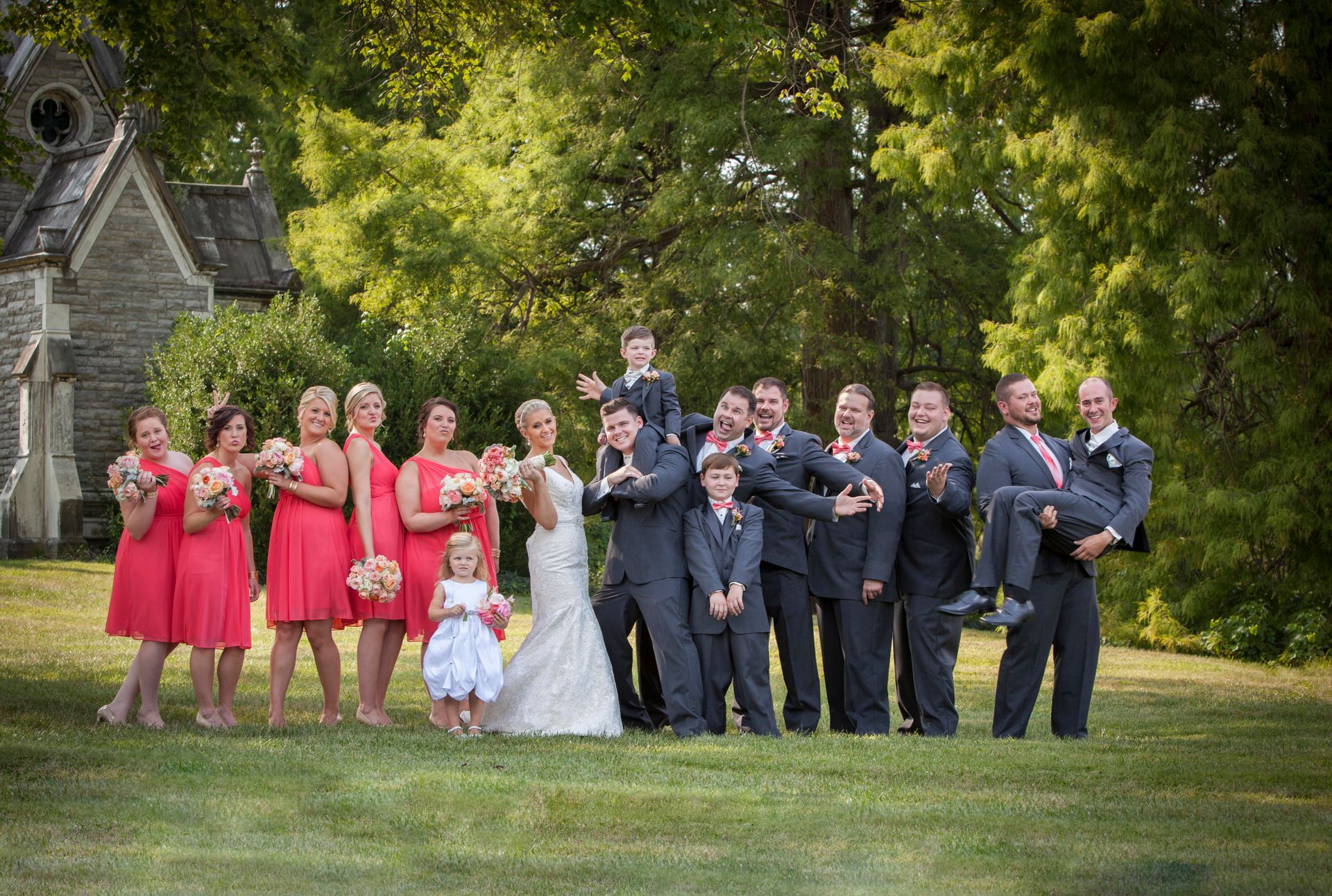 Wedding party posing on a grassy lawn, with bridesmaids in red and groomsmen in navy suits.
