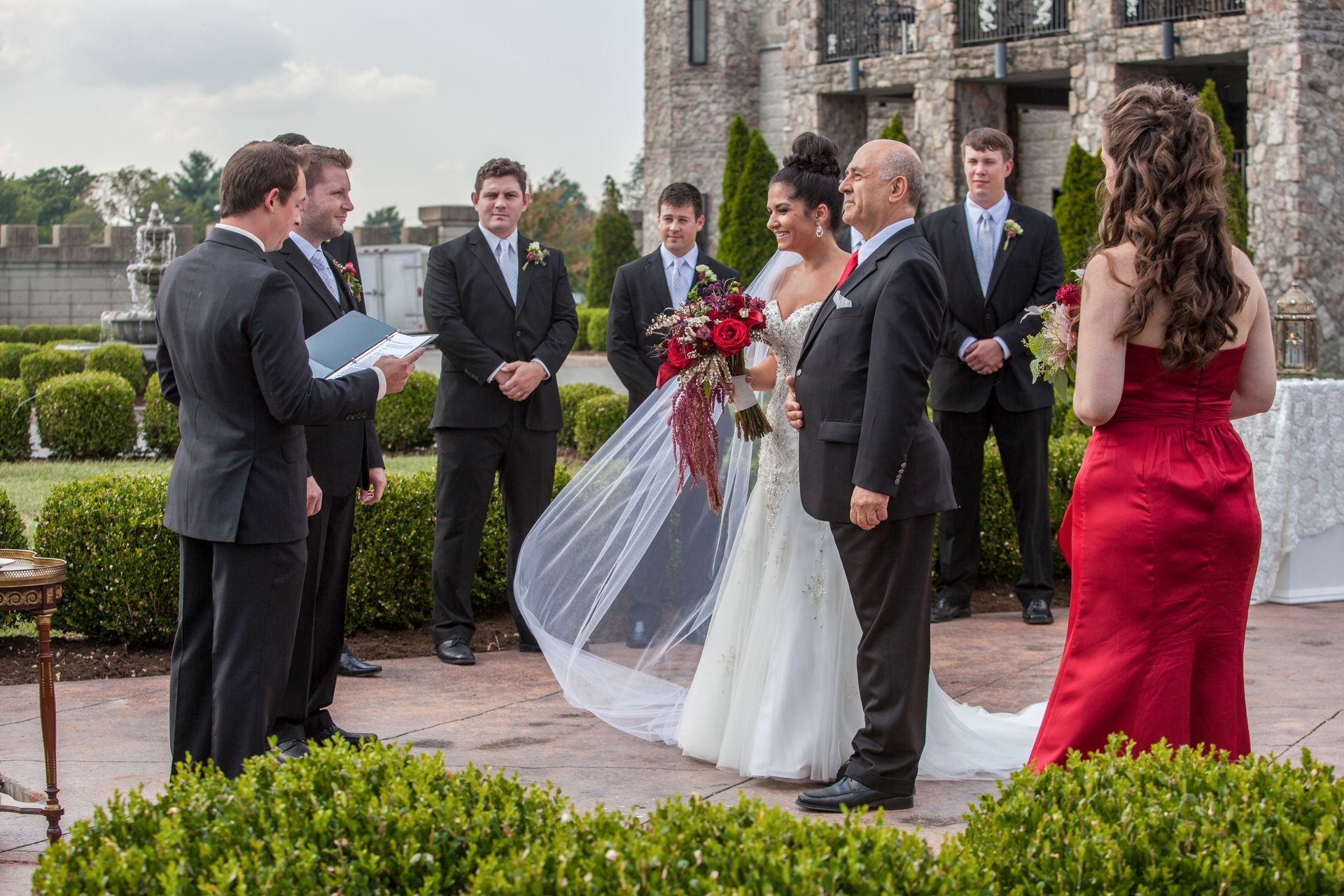 Outdoor wedding ceremony with bride and groom, officiant, and guests in formal attire