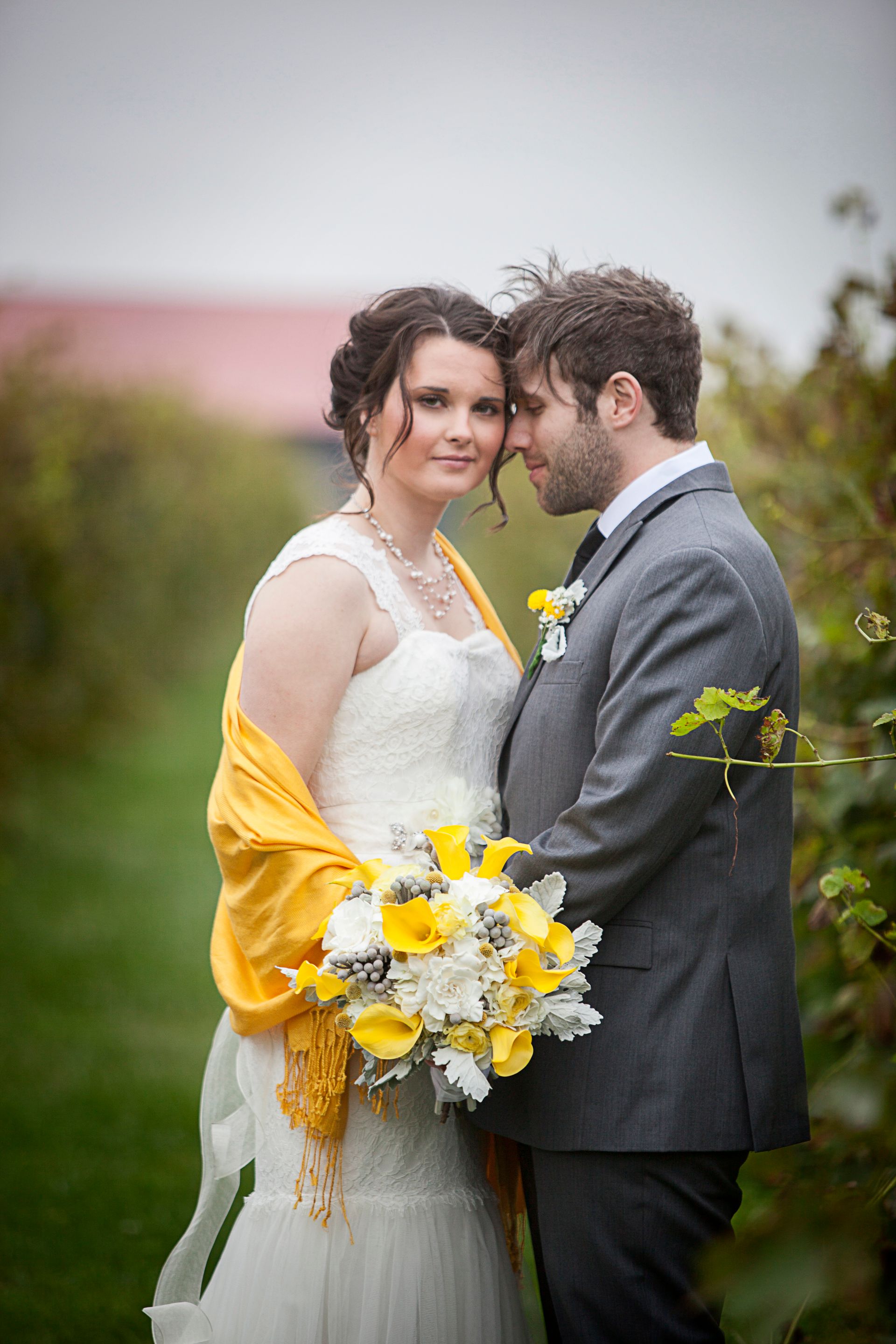 Bride and groom standing together outdoors, holding a yellow-and-white bouquet