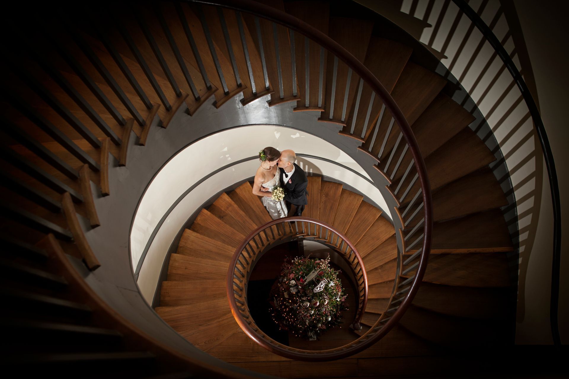 Top-down spiral staircase with two people standing near the center, warm wood steps and white inner walls