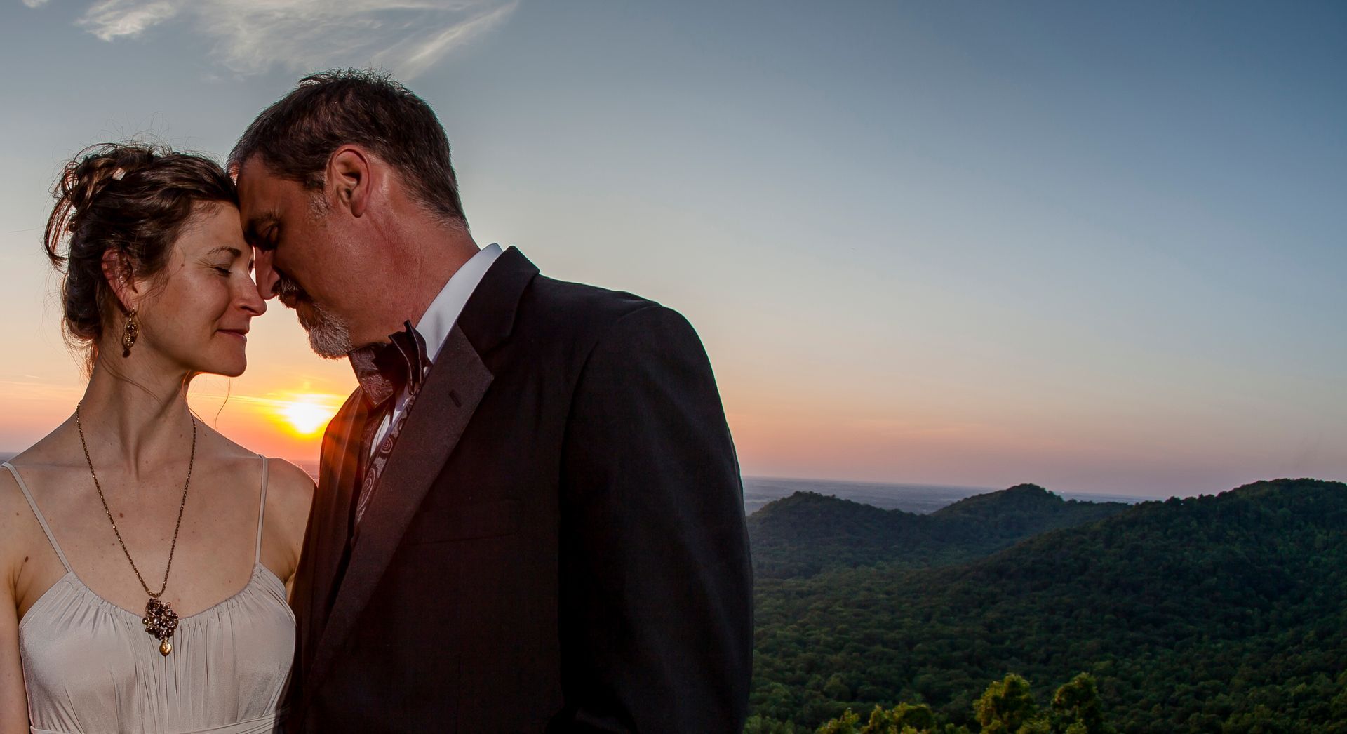 Couple leaning forehead-to-forehead at sunset over rolling green hills