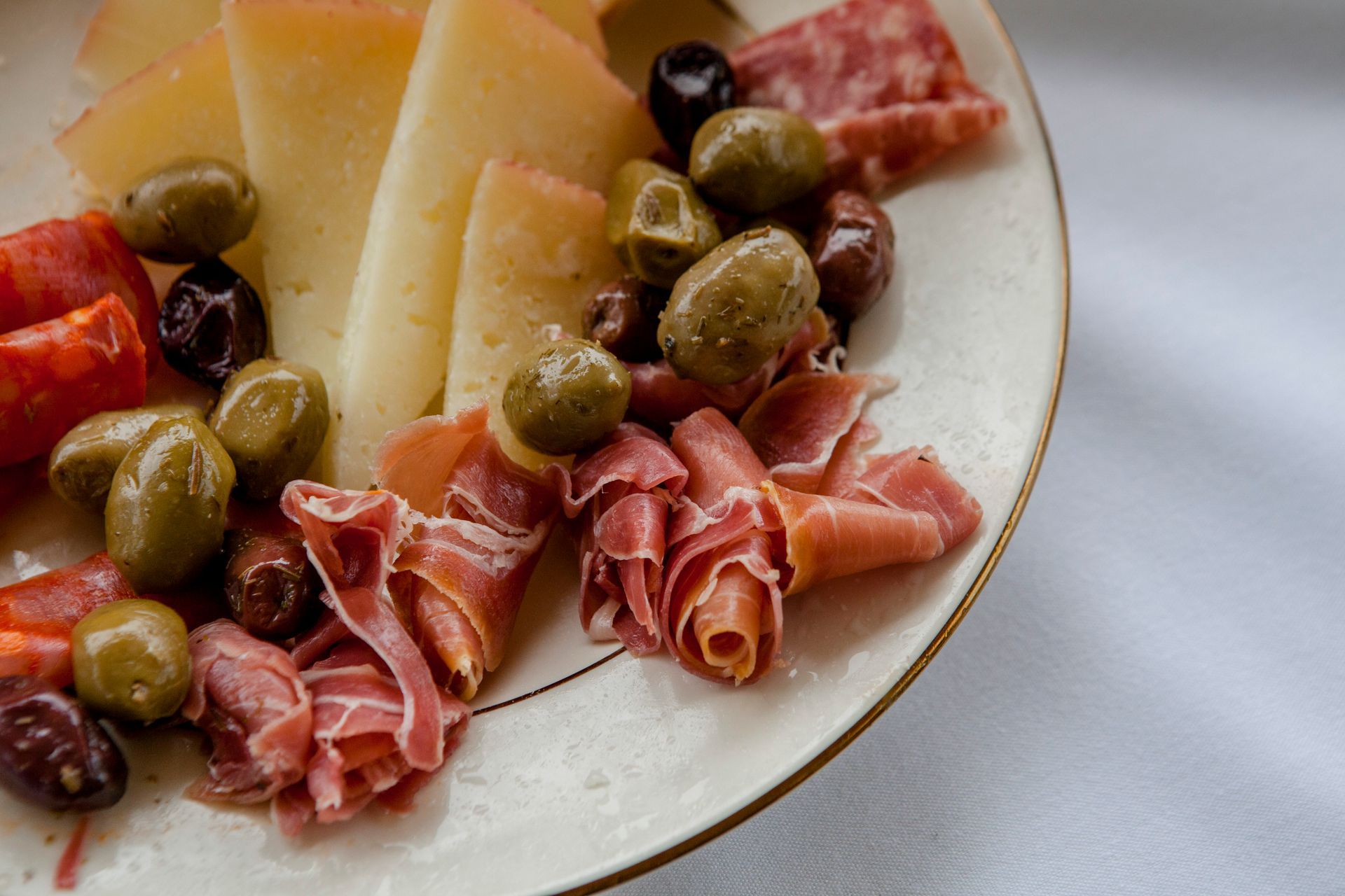 Charcuterie plate with sliced cheese, olives, and cured meats on a white plate