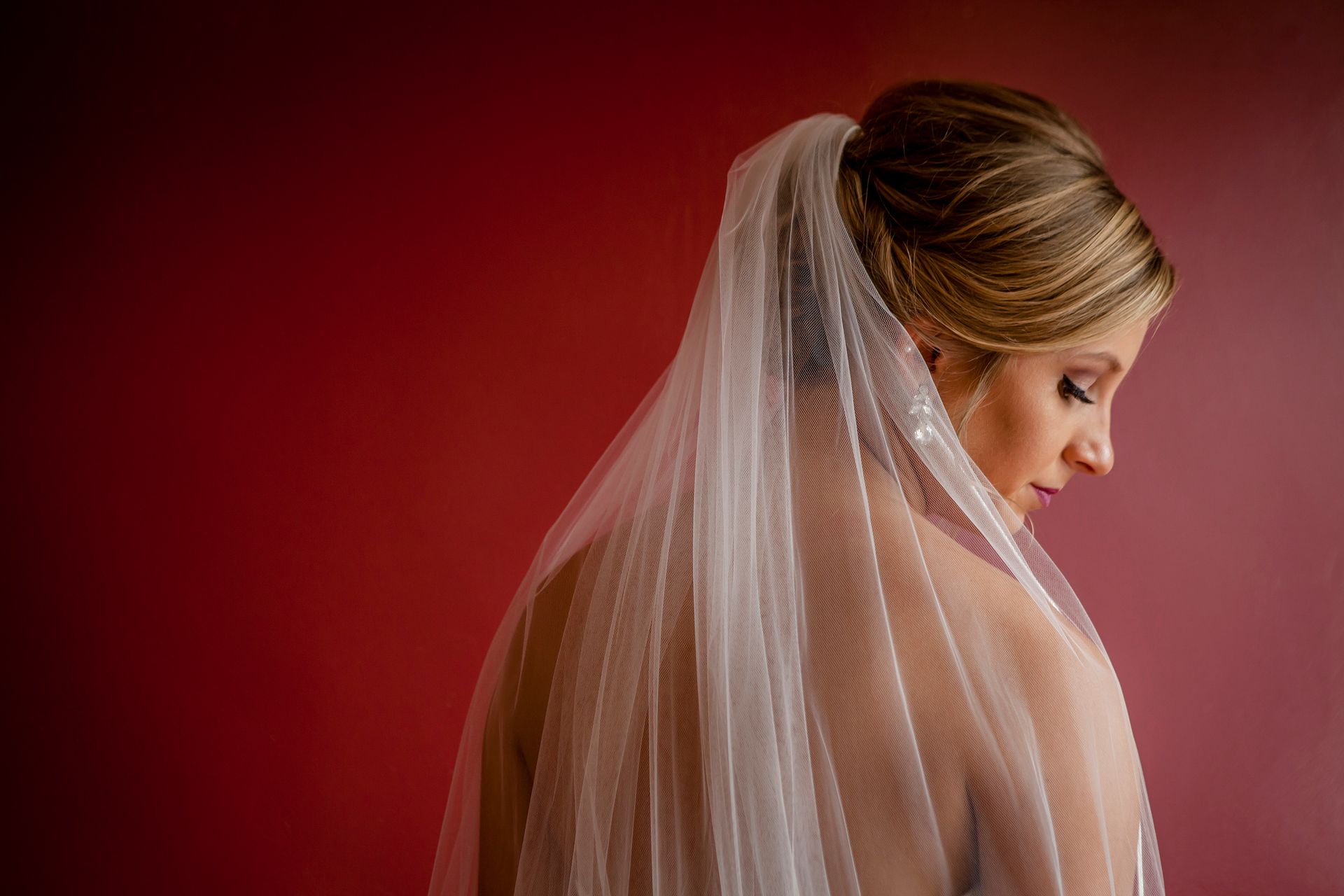 Bride in profile with a white veil against a deep red background