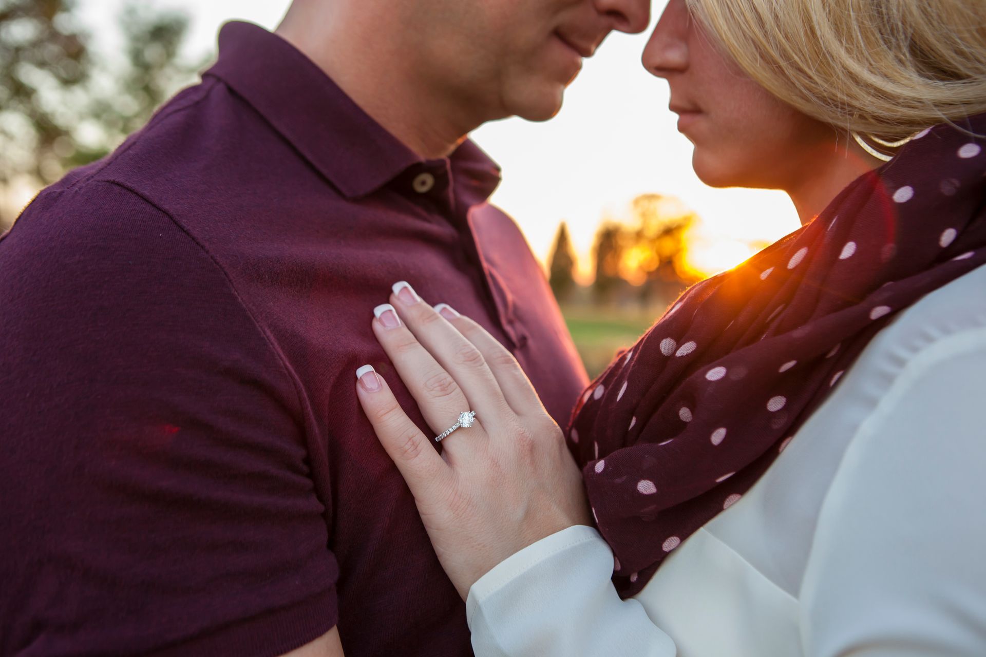 Couple embracing outdoors at sunset, woman’s hand with engagement ring on man’s chest