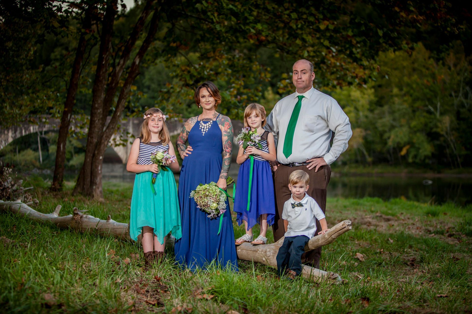 Formal family portrait outdoors by a pond, with three children in blue and green.