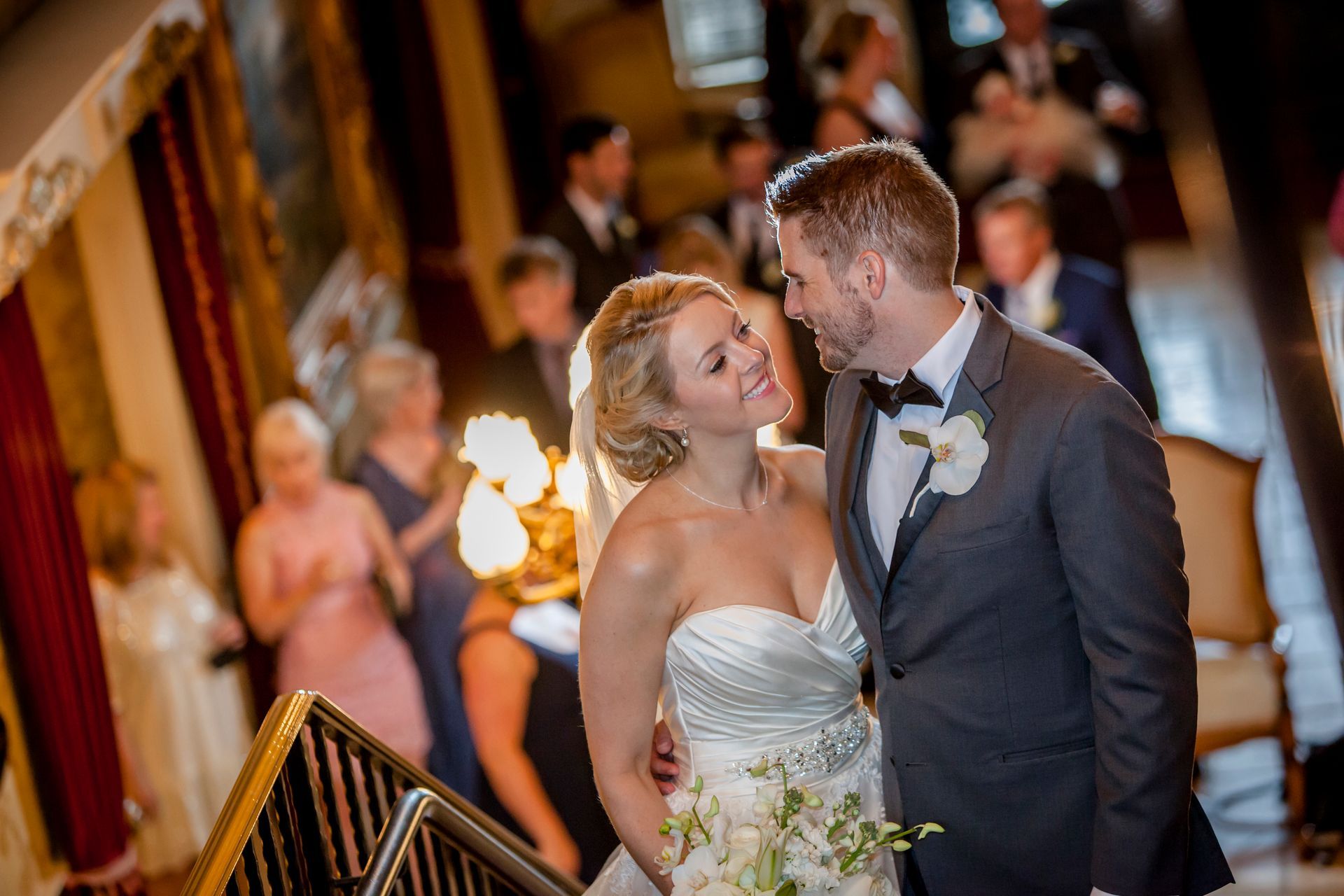 Bride and groom sharing a kiss at the top of a staircase, with guests blurred in the background.
