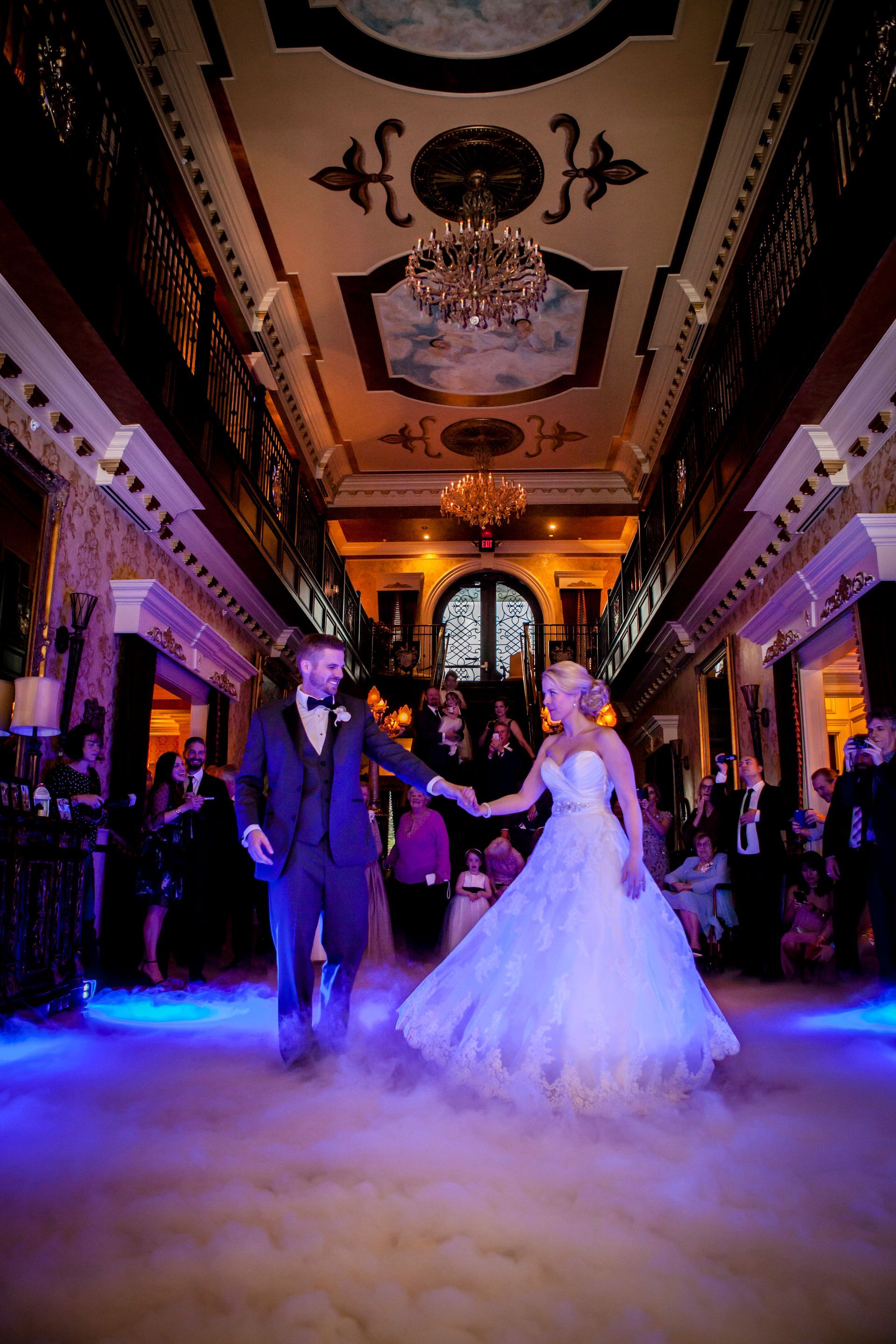 Couple dancing in a grand, chandelier-lit ballroom with blue-purple floor lighting
